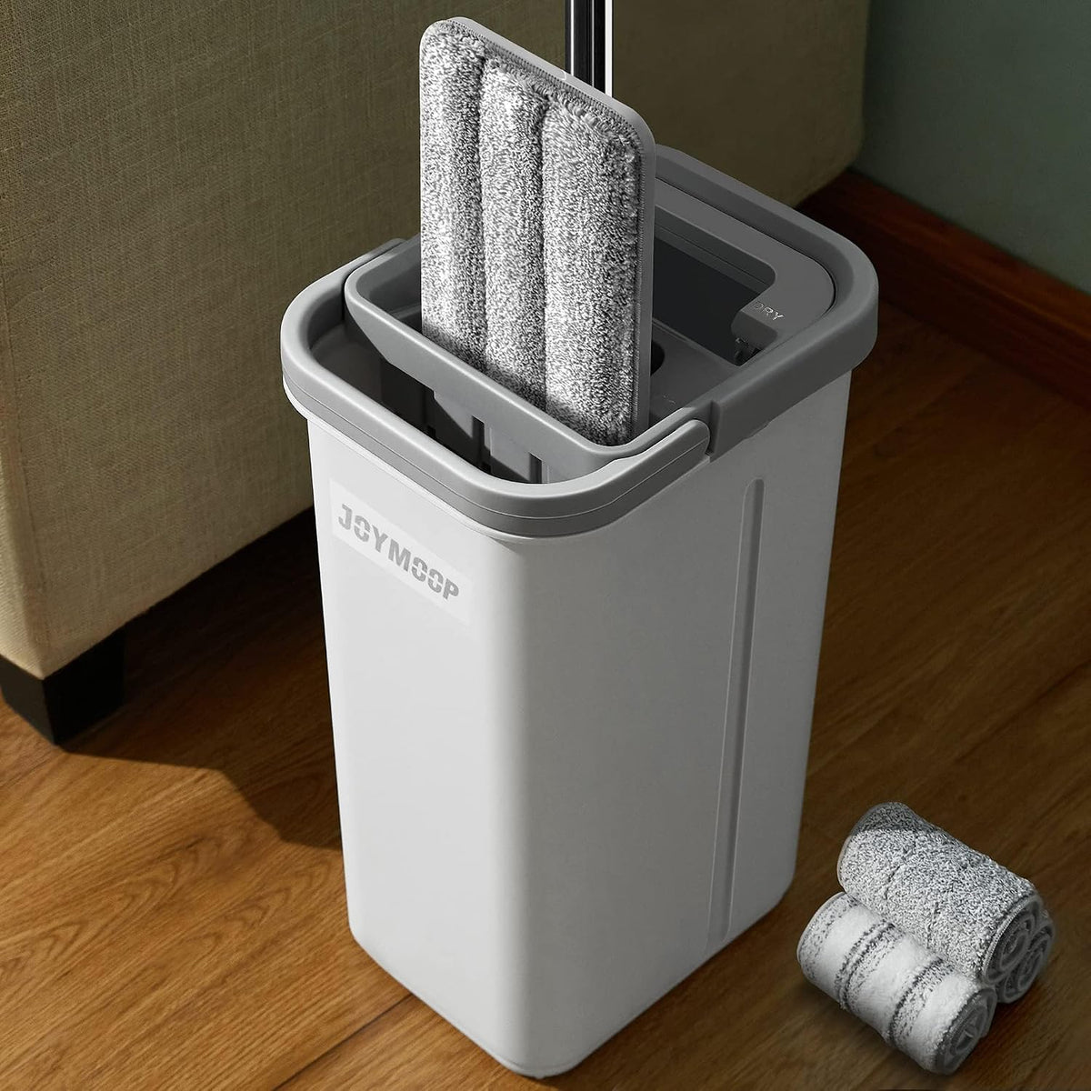Gray mop bucket with interchangeable mop heads on a wooden floor.