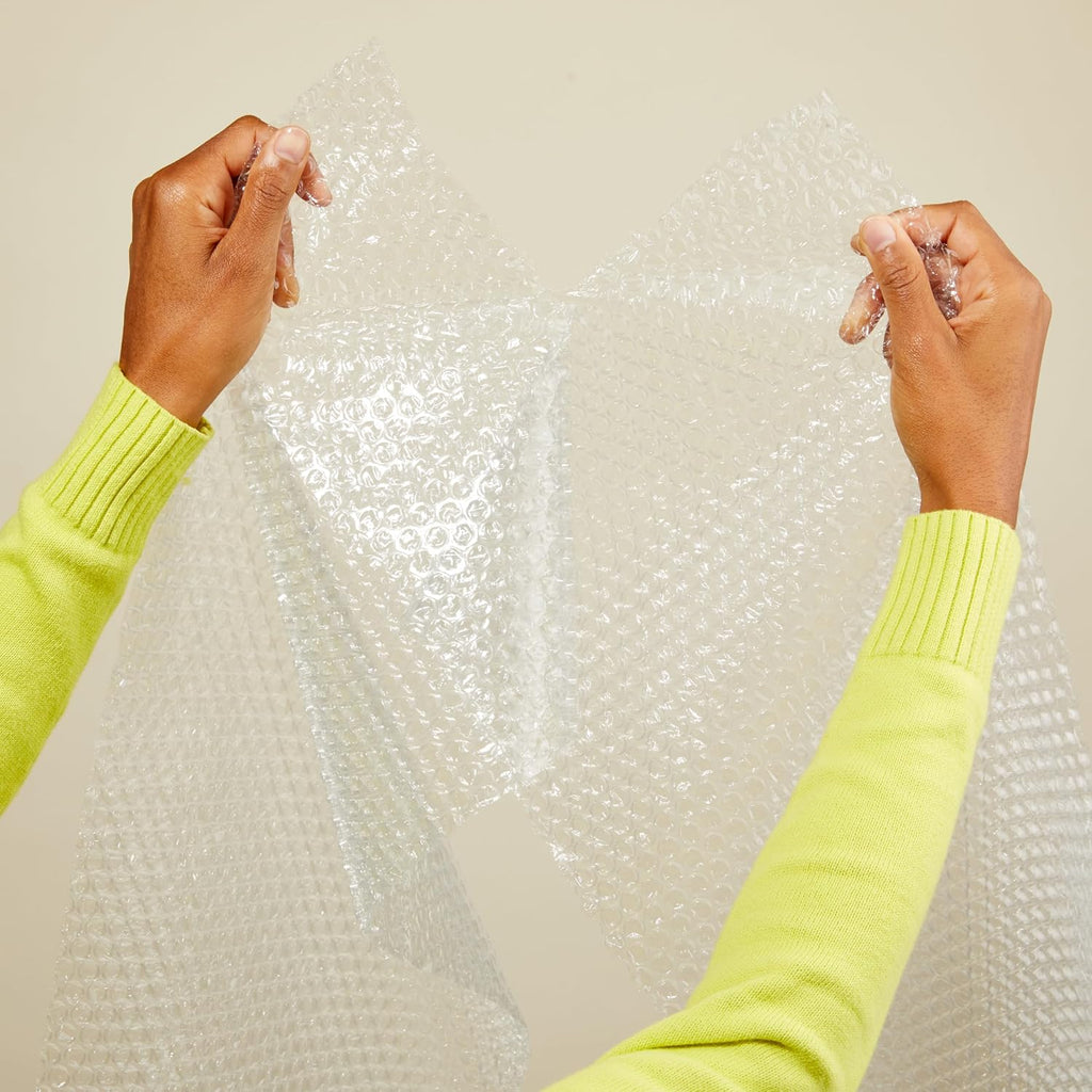 Person wearing a bright green sweater holding bubble wrap against a neutral background